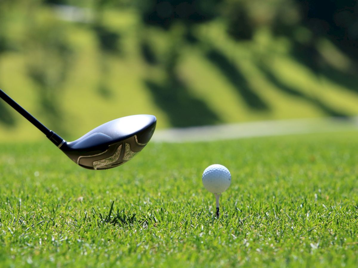 A golf club is about to hit a golf ball on a tee, set on a green grass field.