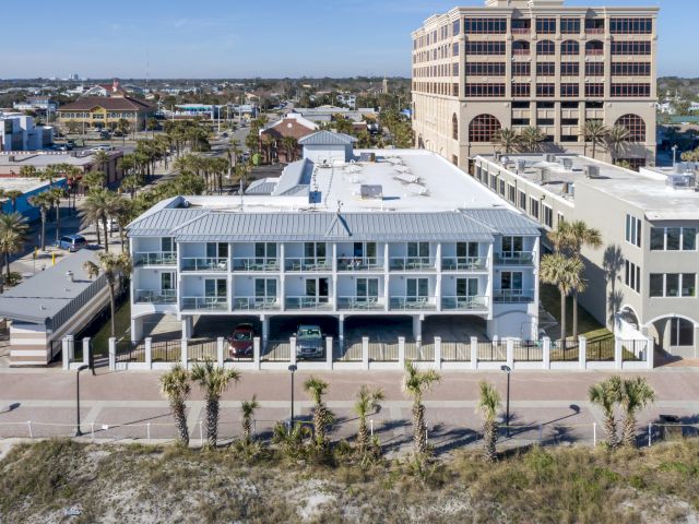 A row of beachside buildings with palm trees in front and other structures visible in the background in a coastal urban area.